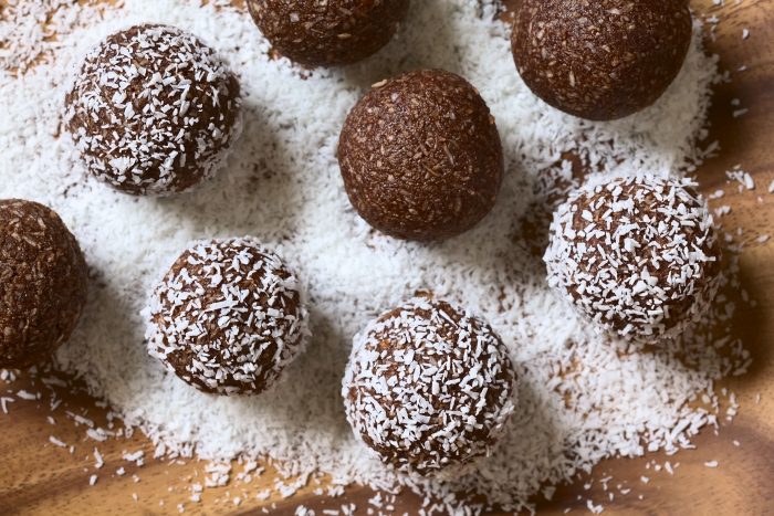 47288353 - coconut rum balls being covered with grated coconut on wooden plate, photographed overhead with natural light (selective focus, focus on the top of the balls)